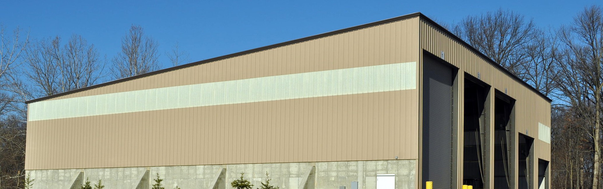 Tan metal warehouse building with four loading dock doors and concrete stem wall