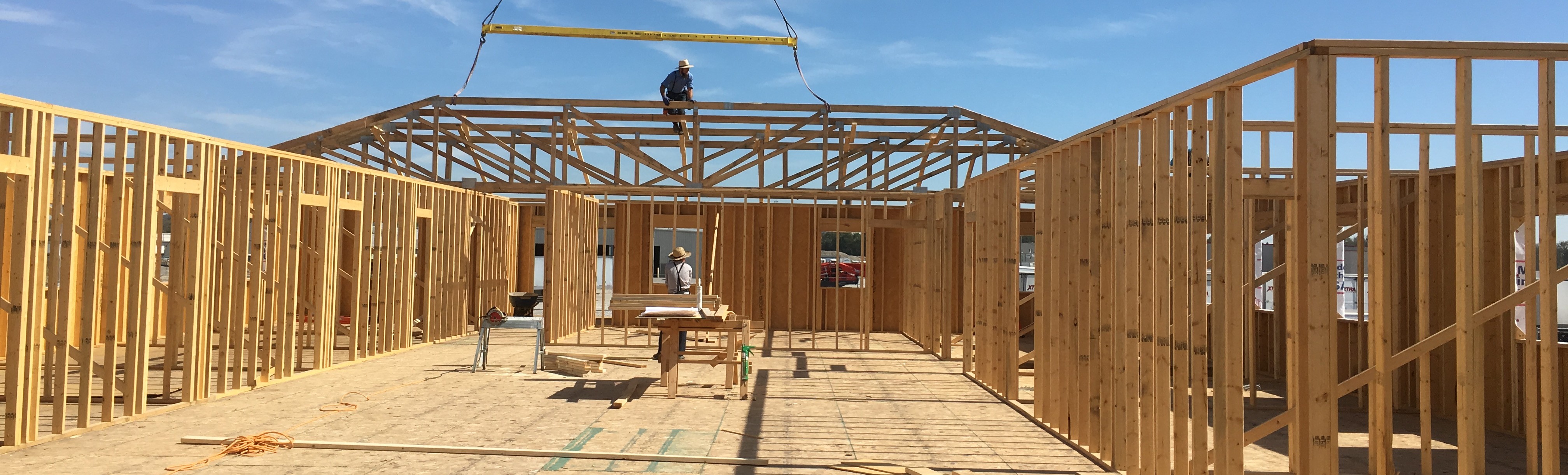 Crane setting a roof truss on a wood-framed commercial building under construction, worker guiding it into place